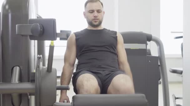 Vista frontal del deportista caucásico enfocado haciendo ejercicio en el gimnasio en el equipo. Retrato de un joven guapo y fuerte entrenando en un club deportivo. Fuerza, masculinidad, estilo de vida . — Vídeos de Stock