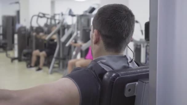 Visão traseira do homem concentrado se exercitando em equipamentos de ginástica. Retrato de jovem forte esportista caucasiano usando máquina de treinamento para músculos da mão. Esporte, masculinidade, força . — Vídeo de Stock