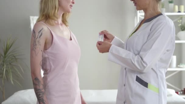 Sidovy av oigenkännlig akupunktör visar nålar och prata med blond smal kvinna i rosa klänning. Självsäker kaukasisk läkare konsulterar tatuerad flicka. Hälsovård, alternativ medicin. — Stockvideo