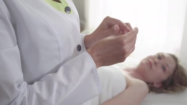 Mãos femininas abrindo agulhas de acupuntura na frente como mulher loira jovem borrada olhando para a câmera de fundo. Retrato de paciente fraco na clínica de acupuntura. Cura, tratamento, medicina . — Vídeo de Stock