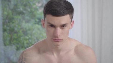 Kendine güvenen yakışıklı beyaz adamın yakın plan portresi başını kaldırıyor ve kameraya bakıyor. Genç esmer çıplak atletik adam içeride poz veriyor. Yaşam tarzı, özgüven, erkeklik..