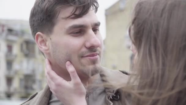 Gros plan d'un beau jeune homme qui parle à sa copine en lui touchant le visage. Heureux petit ami caucasien sortir ensemble avec femme brune méconnaissable en plein air le jour nuageux venteux. Concept d'amour. — Video