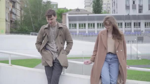 Portrait de timide homme et femme caucasien touchant les mains comme debout à l'extérieur sur la rue de la ville. Jeune couple amoureux sortir ensemble le jour venteux. Flirt, amour, loisir, style de vie. — Video