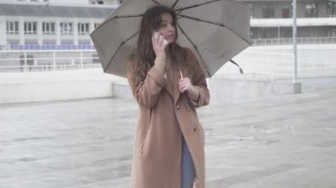 Pozitif genç beyaz kadın telefonda konuşuyor, birine el sallıyor ve gidiyor. Neşeli, güzel esmer kız yağmurlu bir günde şehir caddesinde arkadaşıyla ya da sevgilisiyle buluşuyor..