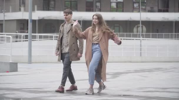 Bred bild av glada unga par dansar utomhus på urban stadsgata. Porträtt av en positiv vit man och kvinna som roar sig tillsammans. Fritid, lycka, dejting, livsstil. — Stockvideo