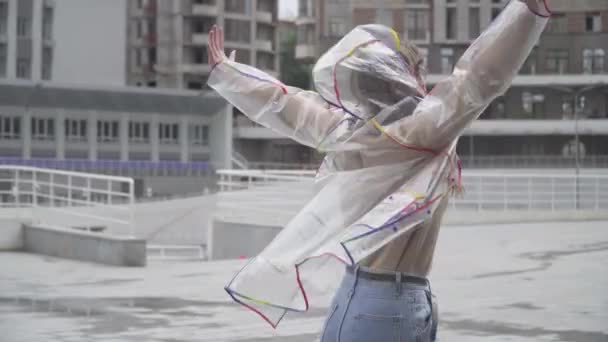 Foto del medio de alegre chica encantadora en gafas de sol y impermeable girando en la calle de la ciudad y riendo. Retrato de una hermosa joven caucásica disfrutando de la temporada de lluvias al aire libre . — Vídeos de Stock