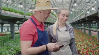 Kendine güvenen beyaz bir adam serada genç ve güzel bir bayana ders veriyor. Profesyonel deneyimli erkek biyolog serada yeni bayan çalışanla konuşuyor. Tarım, biyoloji.