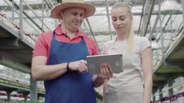 Beyaz adamın tablet ekranda genç ve güzel bir kadına bir şey gösterdiğine eminim. Serada dikilen ve sohbet eden erkek ve kadın meslektaşların portresi.