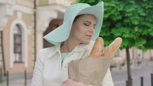 우아 한 여성을 가까이 서 본 결과맛있는 바게트 냄새가 나고 빵을 먹고 있었다. 여름에 도시의 거리에 모습을 드러낸 자신감 넘치는 백인 여성의 모습. 관광의 개념. — 비디오