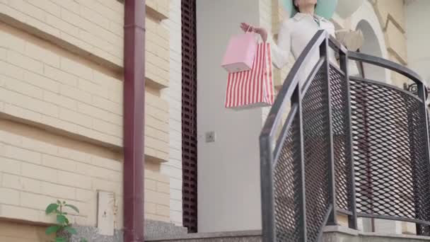 Mujer feliz y segura bajando las escaleras después de ir de compras. Retrato de bella dama caucásica sonriente en elegante abrigo y sombrero saliendo de tienda con bolsos. Moda, estilo, elegancia, estilo de vida . — Vídeo de stock