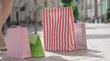 Yüksek topuklu giyen beyaz bir kadın alışveriş çantalarını alıp şehir caddesinde duruyor ve gidiyor. Zarif, zarif bayan alışverişçinin ince bacakları alışverişlerle uzaklaşıyor..