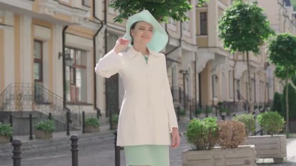 Mujer elegante disfrutando de un día soleado en la ciudad extranjera. Retrato de una encantadora turista caucásica parada al aire libre y sonriente. Feliz dama de sombrero y abrigo blanco posando en viaje europeo . — Vídeos de Stock