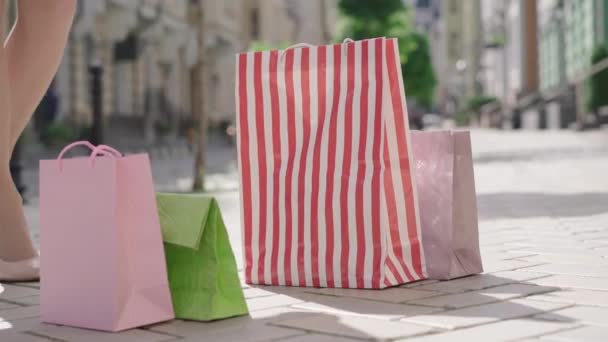 Oigenkännlig vit kvinna i högklackat tar shoppingväskor står på stadens gata och lämnar. Smala ben av eleganta kvinnliga shoppare gå iväg med inköp. — Stockvideo