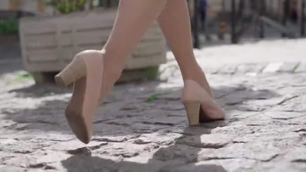 在阳光明媚的城市里，穿着米色高跟鞋的自信的高加索女人沿着人行道走着，摄像机跟随着她的脚步声。难以辨认的时髦女士在户外散步.自信、优雅、时尚. — 图库视频影像