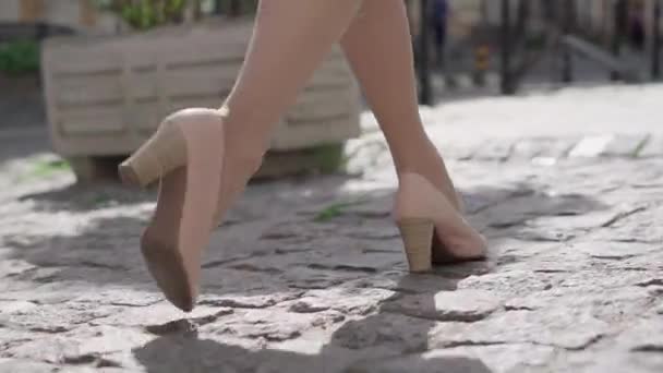 Camera segue piedi di donna caucasica fiduciosa in beige tacchi alti a piedi lungo la strada asfaltata nella giornata di sole in città. Irriconoscibile signora elegante passeggiare all'aperto. Fiducia, eleganza, moda. — Video Stock