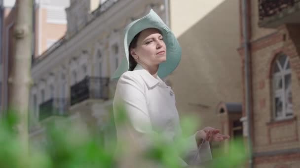 Mellanslag porträtt av glad elegant kvinna beundrar flaska vitt vin utomhus. Leende vit dam i hatt stående på stadens gata med alkohol i händerna. Fritid, livsstil, rikedom. — Stockvideo
