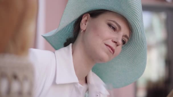 Close-up de mulher caucasiana meio-adulto atraente em chapéu elegante beber vinho tinto durante a leitura. Retrato da senhora bonita elegante que aprecia o dia ensolarado do verão ao ar livre. Lazer, hobby . — Vídeo de Stock