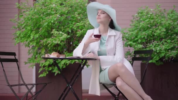 Amplio retrato de una mujer elegante bebiendo vino tinto y pensando. Elegante mujer turista caucásica descansando en la cafetería al aire libre en el día soleado. Soledad, estilo de vida, ocio, turismo . — Vídeos de Stock