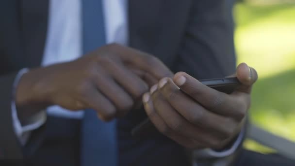Gros plan des mains masculines afro-américaines à l'aide d'un smartphone. Messagerie d'homme d'affaires méconnaissable en ligne dans le chat sans fil. Jeune homme inconnu assis sur un banc dans un parc d'été ensoleillé. — Video