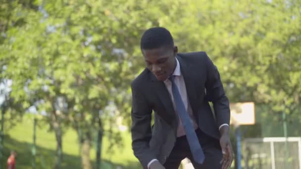 Homem afro-americano positivo confiante jogando basquete ao ar livre. Retrato de homem concentrado em terno de negócios formal desfrutando de pausa no parque no dia ensolarado de verão. Lazer, alegria, descanso, estilo de vida . — Vídeo de Stock