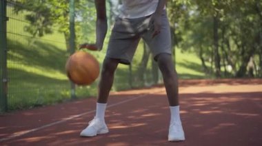 Genç, tanınmayan Afrikalı Amerikalı basketbolcu sahada topa vuruyor. Güneşli bir yaz gününde açık havada spor eğitimi alan üniversite öğrencisi. Yaşam tarzı, spor, hobi.
