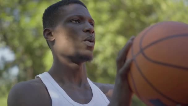 Nahaufnahme eines konzentrierten afroamerikanischen Sportlers, der Ball in Basketballkorb wirft. Porträt eines entschlossenen jungen Mannes, der an einem Sommertag auf dem Außenplatz trainieren will. — Stockvideo