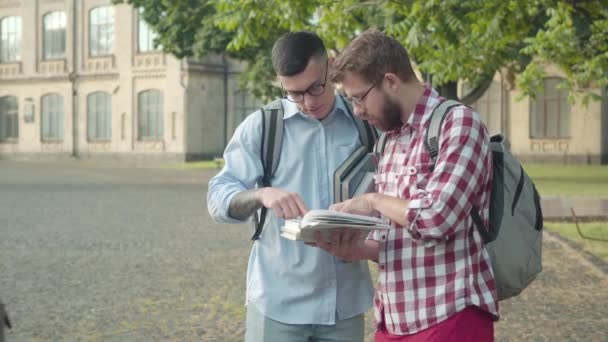 Absorbed smart boys discussing studying in college yard as female groupmates passing by. Portrait of Caucasian male nerds ignoring gorgeous girls in university. Lifestyle concept. — Stock Video