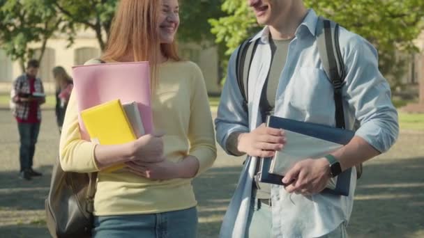 Femme rousse souriante parlant avec un homme méconnaissable dans la cour de l'université. Portrait d'étudiants caucasiens positifs flirtant le jour ensoleillé de l'été. Joie, style de vie, éducation, bonheur. — Video