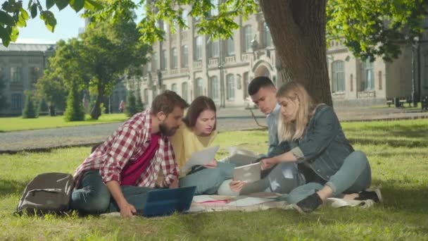 Donna caucasica bionda che mostra qualcosa su tablet ai compagni di gruppo interessati. Studenti maschi e femmine che studiano all'aperto nel cortile soleggiato del campus. Vita universitaria, istruzione, intelligenza. — Video Stock