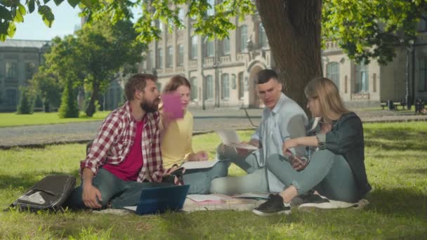 Étudiants caucasiens nerveux se disputant à l'extérieur. Quatre jeunes hommes et femmes criant et gesticulant émotionnellement alors qu'ils étudiaient sur la cour verte ensoleillée de l'université. Conflit, problème du travail d'équipe. — Video