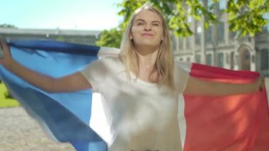 Sarışın, beyaz bir kadın üniversite bahçesinde Fransız bayrağıyla dalgalanıyor. Çalışmaktan zevk alan çekici genç kız öğrencinin portresi. Uluslararası eğitim, zeka, yaşam tarzı kavramı.