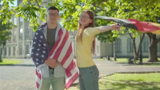 Portret van een gelukkige Amerikaanse studente, gehuld in een nationale vlag, met een glimlachende, mooie vrouw met uitgespreide handen die de Franse vlag vasthoudt. Internationaal onderwijs, patriottisme, intelligentie. — Stockvideo