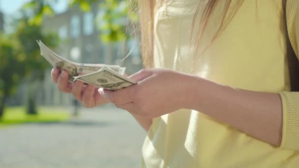 Primer plano de las manos caucásicas femeninas contando dólares. Mujer joven irreconocible calculando los ingresos en el patio de la universidad. Concepto independiente, estudiantes de trabajo, estilo de vida . — Vídeo de stock