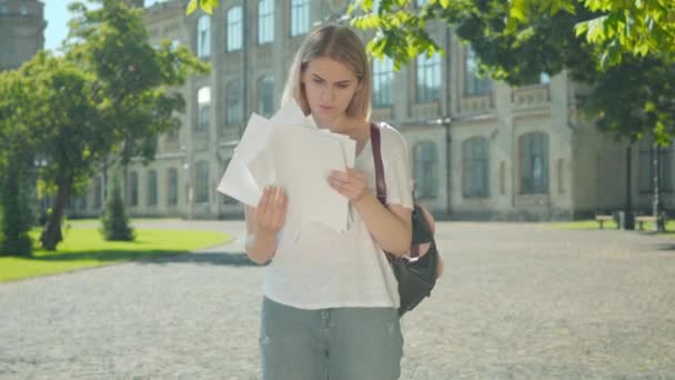 Joven alegre feliz comprobando los resultados de las pruebas, tirando papeles y girando en el patio de la universidad. Retrato de la alegre estudiante caucásica recibiendo buenas noticias en el soleado día de verano . — Vídeo de stock