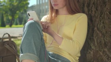 Açık havada güneşli bir günde kulaklıkla müzik dinleyen tanınmamış genç bir üniversite öğrencisi. Kafkasyalı rahat bir kız üniversite bahçesinde dinleniyor. Hobi, eğlence, yaşam tarzı.