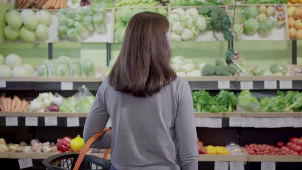 Vista posterior de la morena mujer caucásica de pie frente a los estantes en la tienda de comestibles la elección de alimentos. Jovencita comprando frutas y verduras orgánicas en el supermercado. Concepto de alimentación saludable . — Vídeos de Stock