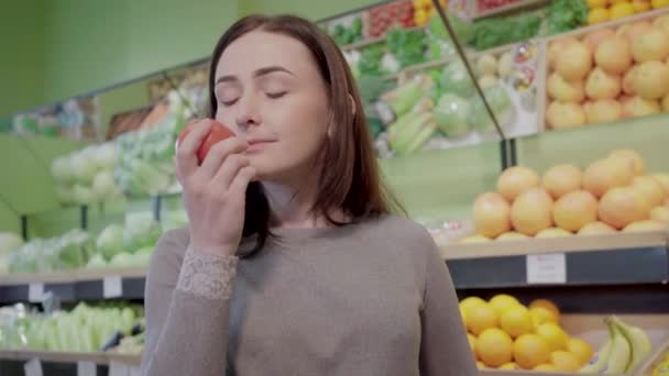 Retrato de cerca de una joven morena oliendo tomate fresco en el supermercado. Hermosa mujer caucásica elegir verduras orgánicas en la tienda de comestibles. Comida saludable, veganismo, estilo de vida vegano . — Vídeos de Stock