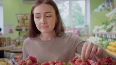 Süpermarkette nefis çilek kokusu alan kendine güvenen beyaz bir kadının portresi. Genç, güzel esmer kız markette lezzetli tatlı yemekleri seçiyor. Vejetaryenlik, yaşam tarzı, sağlıklı beslenme.