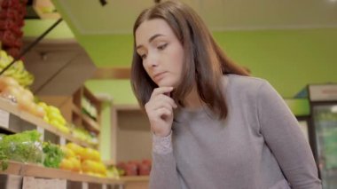 Bakkalda meyve seçen düşünceli genç bir kadın. Marketten pomelo citrus alan güzel esmer kızın portresi. Sağlıklı gıda, yaşam tarzı, veganlık.