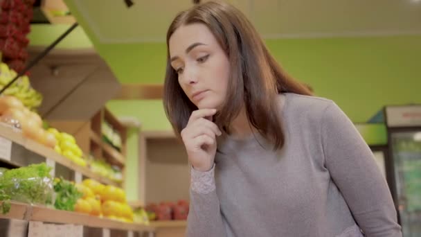 Mujer joven reflexiva elegir frutas en la tienda de comestibles. Retrato de una hermosa chica morena tomando cítricos pomelo para comprar en el supermercado. Comida saludable, estilo de vida, veganismo . — Vídeo de stock