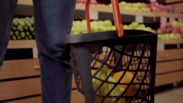 Cámara se mueve desde la cesta de la compra a la cara sonriente de la joven hermosa mujer mirando a la cámara. Retrato de la encantadora chica morena posando en el supermercado con compras. Comida saludable, estilo de vida vegano . — Vídeo de stock