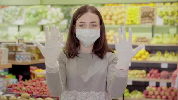 Morena mujer caucásica posando en el supermercado usando mascarilla facial y guantes protectores. Retrato de una joven seria comprando productos en el supermercado en el bloqueo pandémico de Covid-19. Estilo de vida del Coronavirus . — Vídeo de stock