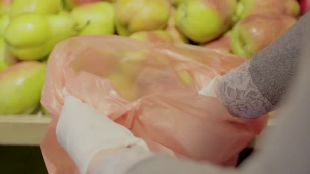Beyaz kadın elleri süpermarkette plastik torbaya armut koyuyor. Covid-19 karantinasında eldiven giymiş tanınmayan bir kadın meyve topluyor. Coronavirus kilitleme, pandemik yaşam tarzı. — Stok video