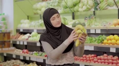 Genç Müslüman kadın markette muz topluyor. Güzel bir bayanın portresi marketten taze organik meyveler seçiyor. Sağlıklı gıda konsepti.