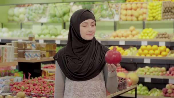 Молодая мусульманка держит гранат и показывает большой палец вверх. Портрет уверенной позитивной девушки, позирующей со свежими вкусными органическими фруктами в продуктовом магазине. — стоковое видео