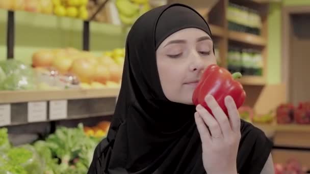 Közelkép fiatal gyönyörű muszlim nő szaga piros harangbors. Portré pozitív aranyos lány hidzsáb kiválasztása zöldségek élelmiszer. Egészséges táplálkozás, bio ételek. — Stock videók