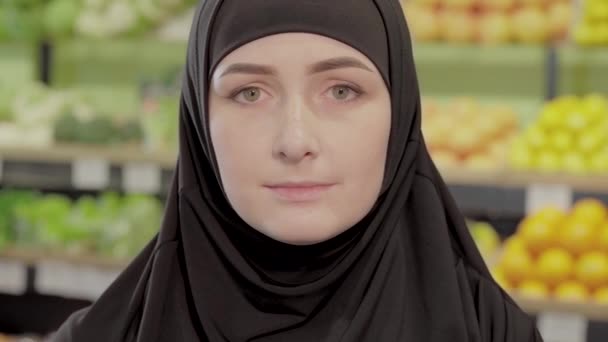 Detailní záběr tvář mladé krásné ženy s oříškově hnědé oči dívá do kamery. Atraktivní muslimská dívka pózující na pozadí polic v supermarketu. — Stock video