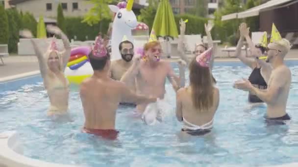 Grupo de jóvenes alegres divirtiéndose en la piscina de agua. Retrato de la pelirroja feliz hombre caucásico celebrando cumpleaños con amigos multirraciales en el complejo hotelero de verano. Ocio, estilo de vida . — Vídeos de Stock