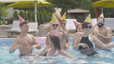 Genç çok ırklı arkadaşlar güneşli bir yaz gününde lüks bir tatil köyünde havuzda dans ediyorlar. Otelde doğum günü partisini kutlayan kendine güvenen erkek ve kadınların portresi. Zenginlik, rahatlık, yaşam tarzı.