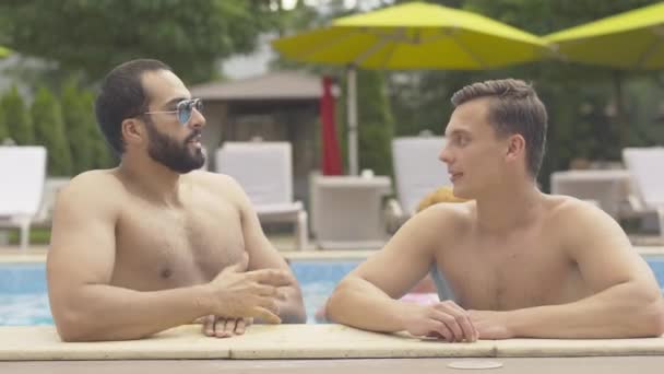 Retrato de hombres jóvenes admirando las piernas delgadas y femeninas que pasan. Guapos amigos masculinos de Oriente Medio y el Cáucaso descansando en un lujoso resort en un soleado día de verano al aire libre junto a la piscina . — Vídeos de Stock